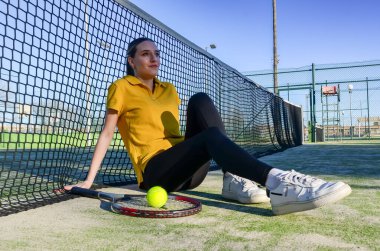 Güneşli bir günde antrenmandan sonra tenis oynayan bayan raketi ve topuyla sahada oturuyor.