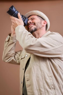Fotoğrafçı, profesyonel dijital kamerayla fotoğraf çekerken konsantre oluyor. Günlük bej ceket ve şapka giyiyor.