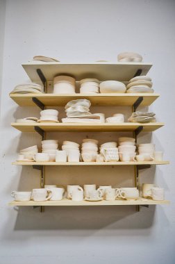 Ahşap raflar seramik atölyesinde seramik parçaların kurutulduğu bir koleksiyon seramik sanatın yapımında kullanılan işçiliğin altını çiziyor.