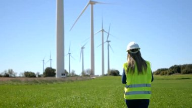 Rüzgar türbinlerine doğru yürüyen mühendis, yenilenebilir enerji üretimini denetliyor
