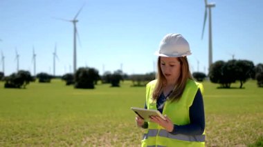 Mühendis, bir rüzgar türbini çiftliğini tablet kullanarak inceliyor.