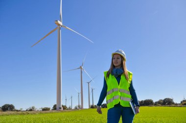 Yenilenebilir enerji üzerinde çalışan endüstri mühendisi bir tabletle bir rüzgar türbini çiftliğini geziyor ve inceliyor.