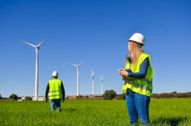 Mühendisler yenilenebilir enerji santralindeki rüzgar türbinlerini inceliyor.