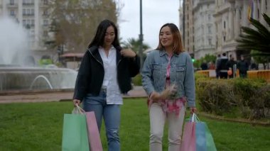 İki bayan arkadaş alışveriş sonrası ellerinde poşetlerle mutlu mesut yürüyüp konuşuyorlar.