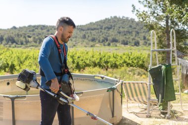 Bahçıvan, güneşli bir meyve bahçesinde, havuzun yanında fırçayla çalışıyor.