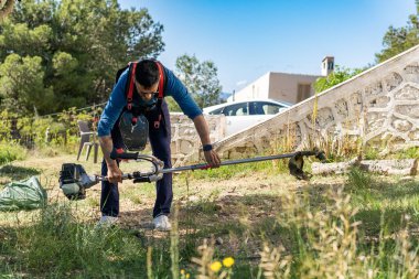Bahçıvan, bir yaz günü bahçedeki yabani otları temizlemek için fırça kullanıyor.