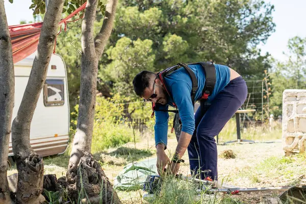 Bahçıvan, karavan ve hamakla bir kampta çim biçmek için fırça hazırlıyor.
