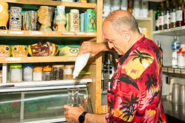 Barmen dikkatle bardağa şurup dökerek canlı tiki barında egzotik kokteyl hazırlıyor.