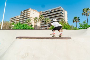 Kask takan ve koruma altında kaykay antrenmanı yapan genç bir çocuk.