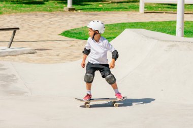 Kaykay parkında kask takıp kaykay antrenmanı yapan bir çocuk.