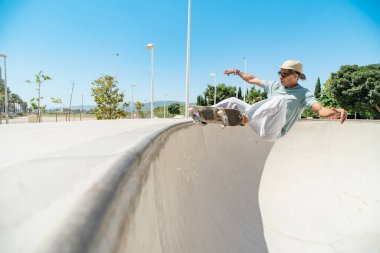 Kaykay yapan genç bir adam, güneşli bir günde bir numara yapıyor.