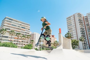 Kentsel bir kaykay parkında scooter numaraları yapan genç bir sporcu.