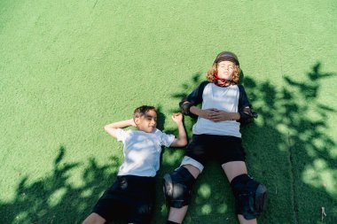 İki genç patenci çimenlerde uzanmış antrenmandan sonra dinleniyor, yaz güneşinin tadını çıkarıyorlar.