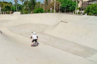 Çocuk kaykay parkında kayarken, güvenlik ve beceri gösterisi yaparken açık hava aktivitelerinin tadını çıkarıyor.
