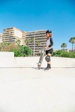 Kaykayını elinde tutan genç bir kaykaycı güvenlik ekipmanı takıyor.