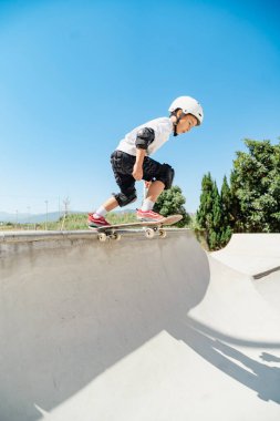 Kaykay parkında kask ve koruyucu giyip kaykay antrenmanı yapan bir çocuk.