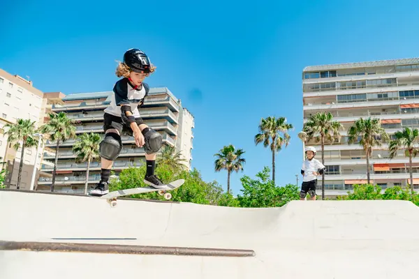 Kaykay parkında kasklı ve korumalı bir şekilde atlayan bir çocuk.
