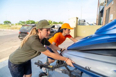 İki kadın tamirci bir jet ski 'yi bakım ve depolama amaçlı bir karavana itiyor.
