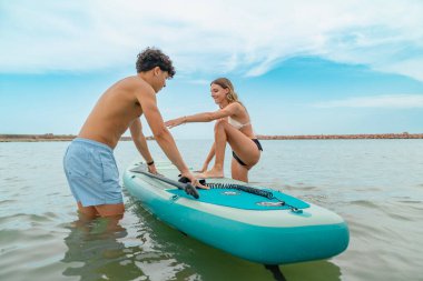 Genç çift ayağa kalkmaya hazırlanıyor. Denizde sörf yapmaya.