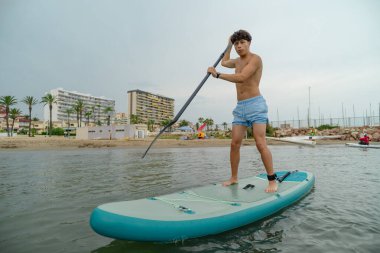 Şehir plajı yakınlarında ayakta sörf yapan bir turist.