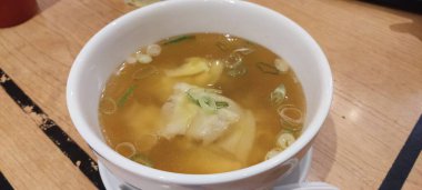 Beyaz kase dokusunda ve arka planında wonton çorbası.