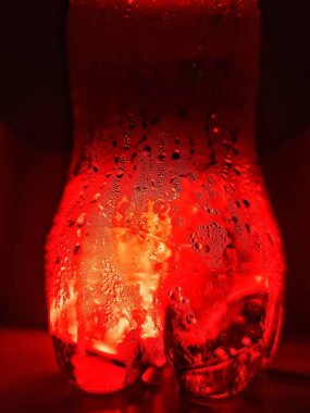 Gazoz suyundan çıkan baloncuklar, kırmızı ışık efektleri, kırmızı ışıkta şişenin üzerine su damlaları. Yakın plan. Gazoz suyundan çıkan kabarcıklar, kırmızı ışık efekti.