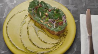 Güzel dekore edilmiş sarı tabakta birkaç yeşil malzemeli tost ve gri bir masanın yanındaki tabağın yanında beyaz bir fincan var..