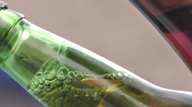 Kapalı yeşil bira şişesinin ağzının detaylı görüntüsü, içinde baloncuklar olan sıvı ve arka planı bulanık..