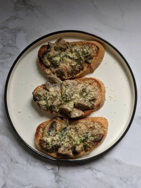 Kızarmış ekmeğin üzerindeki kremalı mantar beyaz tabakta servis edilir.