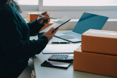 Girişim KOBİ küçük işletme girişimcisi önlük giyen Asyalı kadın dizüstü bilgisayar ve kutu kullanarak çevrimiçi müşterilere, çevrimiçi sme iş fikirlerine satış hazırlamak için siparişleri alır ve gözden geçirir.