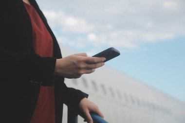 Uluslararası havaalanındaki genç Asyalı kadın, cep telefonu kullanıyor ve uçuş bilgilerini kontrol ediyor.