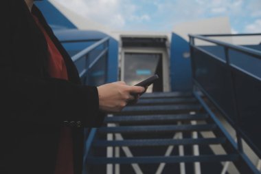 Uluslararası havaalanındaki genç Asyalı kadın, cep telefonu kullanıyor ve uçuş bilgilerini kontrol ediyor.