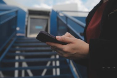 Uluslararası havaalanındaki genç Asyalı kadın, cep telefonu kullanıyor ve uçuş bilgilerini kontrol ediyor.