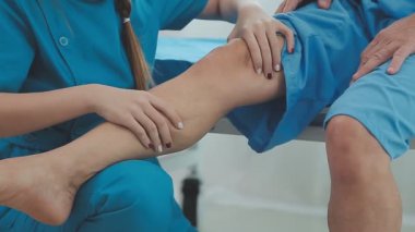 Doktor bacağıyla hastanın bacağını muayene ediyor.