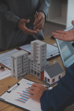 Emlak sektörünü dengelemek. Emlakçı ev tasarımını ve satın alma anlaşmasını görmek için ev tarzını anlatıyor. Modern ofiste ahşap ev.