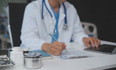 Önlüklü profesyonel ve odaklanmış Asyalı kadın bir doktor hastanede bilgisayarında tıbbi araştırmaları okuyor ve çalışıyor..