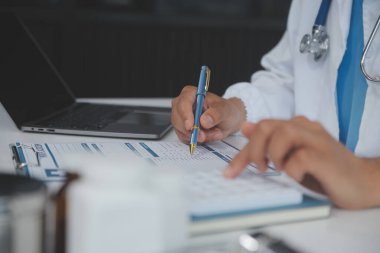 Önlüklü profesyonel ve odaklanmış Asyalı kadın bir doktor hastanede bilgisayarında tıbbi araştırmaları okuyor ve çalışıyor..