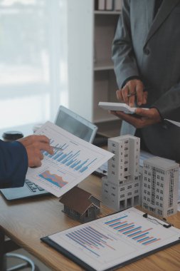 Emlak sektörünü dengelemek. Emlakçı ev tasarımını ve satın alma anlaşmasını görmek için ev tarzını anlatıyor. Modern ofiste ahşap ev.