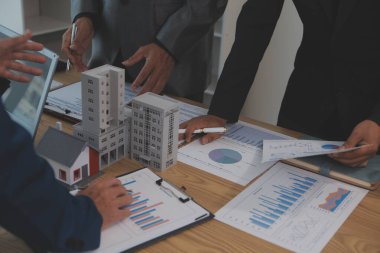 Emlak sektörünü dengelemek. Emlakçı ev tasarımını ve satın alma anlaşmasını görmek için ev tarzını anlatıyor. Modern ofiste ahşap ev.