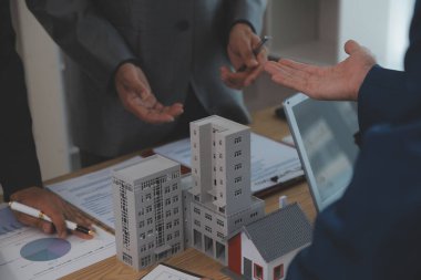Emlak sektörünü dengelemek. Emlakçı ev tasarımını ve satın alma anlaşmasını görmek için ev tarzını anlatıyor. Modern ofiste ahşap ev.
