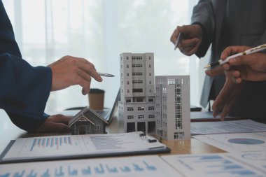 Emlak sektörünü dengelemek. Emlakçı ev tasarımını ve satın alma anlaşmasını görmek için ev tarzını anlatıyor. Modern ofiste ahşap ev.