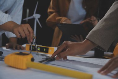 Toplantı odasında inşaat planları üzerinde çalışan çok ırklı mimarlardan oluşan bir ekip. Mühendisler ofiste proje üzerinde tartışıyorlar. Olgun iş adamı ve kadın masanın etrafında durmuş plan üzerinde çalışıyorlar..