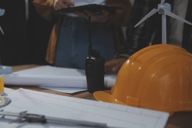 Toplantı odasında inşaat planları üzerinde çalışan çok ırklı mimarlardan oluşan bir ekip. Mühendisler ofiste proje üzerinde tartışıyorlar. Olgun iş adamı ve kadın masanın etrafında durmuş plan üzerinde çalışıyorlar..