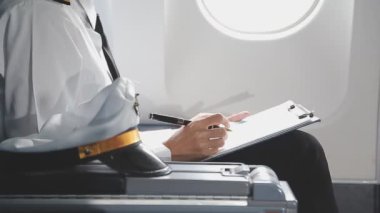 Not defteri ve kalemle beyaz takım elbiseli genç bir kadın uçağın penceresinin yanında oturuyor..