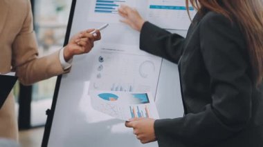 İş kadını elinde kalem tutarak ofisteki iş ekibinin ekranına işaret ediyor.