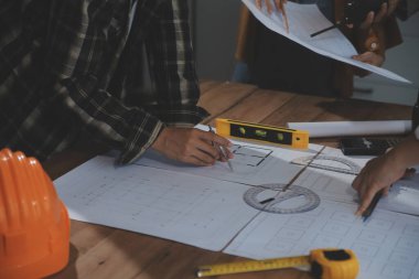 Toplantı odasında inşaat planları üzerinde çalışan çok ırklı mimarlardan oluşan bir ekip. Mühendisler ofiste proje üzerinde tartışıyorlar. Olgun iş adamı ve kadın masanın etrafında durmuş plan üzerinde çalışıyorlar..