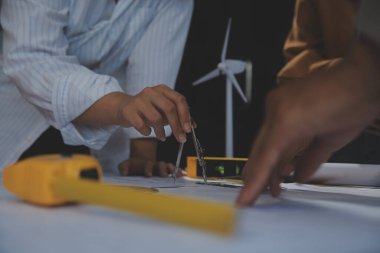 Toplantı odasında inşaat planları üzerinde çalışan çok ırklı mimarlardan oluşan bir ekip. Mühendisler ofiste proje üzerinde tartışıyorlar. Olgun iş adamı ve kadın masanın etrafında durmuş plan üzerinde çalışıyorlar..