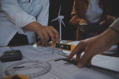 Toplantı odasında inşaat planları üzerinde çalışan çok ırklı mimarlardan oluşan bir ekip. Mühendisler ofiste proje üzerinde tartışıyorlar. Olgun iş adamı ve kadın masanın etrafında durmuş plan üzerinde çalışıyorlar..