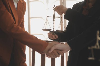 Avukat, müvekkil ile evraklar, sözleşmeler, anlaşmalar, iş birliği anlaşmaları hakkında el sıkışıyor avukatın masasında bir kadın müvekkil ve masada bir çekiç.