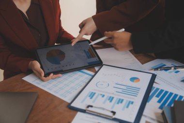 Group of confident business people point to graphs and charts to analyze market data, balance sheet, account, net profit to plan new sales strategies to increase production capacity.